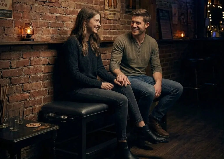 A couple sits on a bench in a bar holding hands